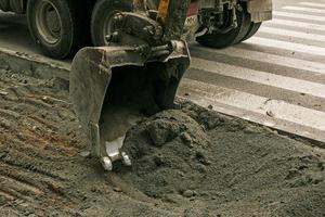 travaux routiers dans la rue de la ville. le godet de la pelle récupère l'ancien revêtement et le charge dans un camion à benne basculante photo