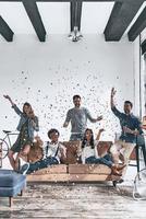 meilleure fête avec les meilleurs amis. groupe de jeunes gens heureux en vêtements décontractés buvant du champagne tout en passant du temps à la maison avec des confettis volant partout photo