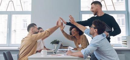 groupe de jeunes confiants en vêtements décontractés intelligents, main dans la main et souriant tout en se réunissant au bureau photo