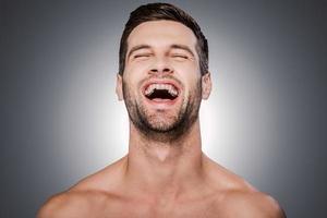 vrai bonheur. portrait d'un beau jeune homme torse nu gardant les yeux fermés et souriant en se tenant debout sur fond gris photo