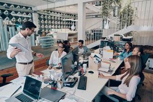 groupe de jeunes gens modernes en vêtements décontractés intelligents discutant des affaires tout en travaillant au bureau photo