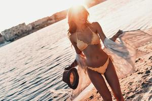 montrant son corps incroyable. jolie jeune femme souriante debout sur la plage à l'extérieur photo