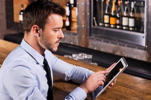 toujours rester en contact. jeune homme confiant en chemise et cravate assis au comptoir du bar et travaillant sur une tablette numérique photo