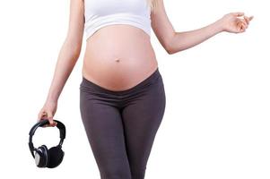 on aime la musique. image recadrée d'une femme enceinte tenant un casque en se tenant debout isolé sur blanc photo