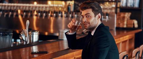 beau jeune homme en costume complet tenant un verre avec une boisson alcoolisée photo