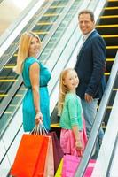 faire du shopping ensemble est une famille joyeuse et amusante tenant des sacs à provisions et regardant par-dessus l'épaule tout en montant par un escalator photo
