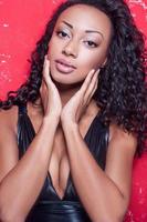 mannequin glamour. belle jeune femme afro-américaine avec maquillage et coiffure posant sur fond rouge photo