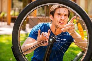 réparer mon vélo. jeune homme confiant fixant son vélo tout en se tenant à l'extérieur et contre la maison photo