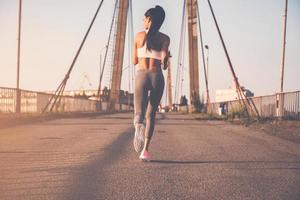 continuez à courir. vue arrière sur toute la longueur de la belle jeune femme en vêtements de sport courant le long du pont photo