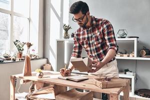 tout vérifier. beau jeune homme écrivant quelque chose dans son organiseur personnel tout en se tenant à l'intérieur photo