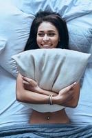 se sentir rafraîchi et plein d'énergie. vue de dessus d'une jeune femme séduisante embrassant un oreiller et souriant en position allongée sur le lit à la maison photo