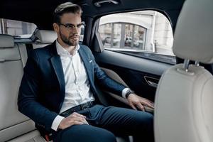 jeune et prospère. beau jeune homme en costume complet regardant loin tout en étant assis dans la voiture photo