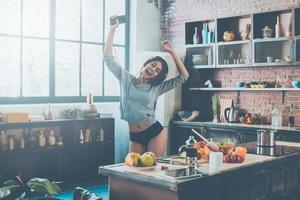 profitant d'une nouvelle belle journée. belle jeune femme métisse au casque dansant debout dans la cuisine à la maison photo