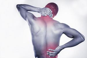 douleur articulaire. vue arrière du jeune homme africain musclé touchant son cou et sa hanche en se tenant debout sur fond gris photo