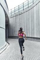 entraînement du matin. vue arrière sur toute la longueur d'une jeune femme en vêtements de sport faisant du jogging pendant l'exercice à l'extérieur photo