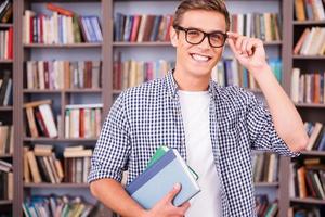 étudiant en bibliothèque. beau jeune homme tenant des livres et souriant debout dans la bibliothèque photo