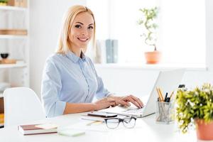 belle femme d'affaires. joyeuse jeune belle femme travaillant sur un ordinateur portable et regardant la caméra avec le sourire alors qu'elle était assise sur son lieu de travail photo