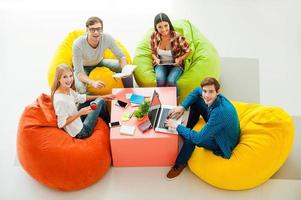 espace de travail créatif. vue de dessus de quatre jeunes gens joyeux travaillant ensemble et levant les yeux assis devant les sacs de haricots colorés photo