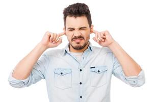 c'est trop fort jeune homme frustré en chemise tenant les doigts dans ses oreilles et gardant les yeux fermés en se tenant debout sur fond blanc photo