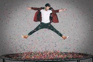 plaisir insouciant. tir en l'air d'un beau jeune homme sautant sur un trampoline avec des confettis tout autour de lui photo
