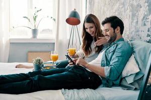 heureux ensemble. beau jeune couple prenant son petit déjeuner tout en passant du temps au lit à la maison photo