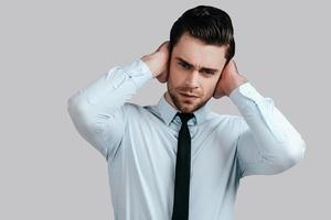 se sentir déprimé. jeune homme frustré en tenues de soirée touchant sa tête avec les mains et regardant la caméra en se tenant debout sur fond gris photo