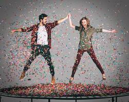 profiter de temps insouciants ensemble. tir en l'air d'un beau jeune couple joyeux sautant sur un trampoline avec des confettis tout autour d'eux photo