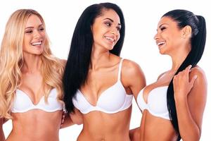 jeune et jolie. trois belles jeunes femmes en lingerie s'embrassant et se regardant avec des sourires en se tenant debout sur fond blanc photo