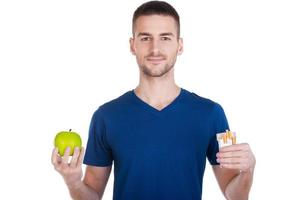 faire le bon choix. jeune homme confiant tenant une pomme dans une main et un paquet de cigarettes dans une autre et isolé sur blanc photo