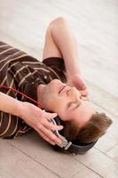 la musique dans ma vie. vue de dessus d'un beau jeune homme au casque écoutant de la musique et gardant les yeux fermés en position couchée sur le sol photo