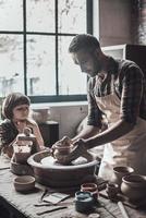 apprendre de nouvelles compétences. jeune homme confiant et petit garçon faisant un pot en céramique sur la classe de poterie photo