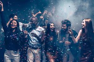 profiter d'une grande fête ensemble. groupe de beaux jeunes lançant des confettis colorés et ayant l'air heureux photo