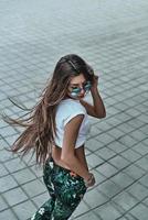 tenue cool. vue de dessus d'une belle jeune femme gardant la main dans les cheveux et regardant par-dessus l'épaule tout en marchant à l'extérieur photo