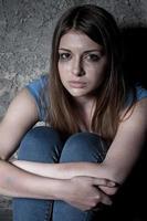 femme désespérée. vue de dessus d'une jeune femme pleurant et regardant la caméra assise contre un mur sombre photo
