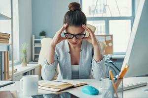 jeune femme stressée en tenue décontractée intelligente gardant la tête dans les mains tout en étant assise au bureau