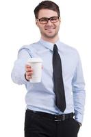prendre une pause. joyeux jeune homme en chemise et cravate tendant une tasse de café en se tenant debout isolé sur blanc photo