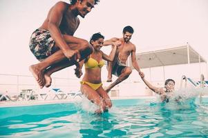 profiter de la fête à la piscine avec des amis. groupe de beaux jeunes qui ont l'air heureux en sautant ensemble dans la piscine photo