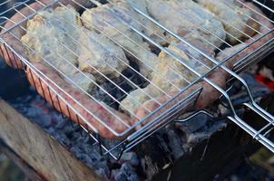 les brochettes d'ailes de poulet sont frites sur le terrain. un barbecue classique en plein air. le processus de friture de la viande sur du charbon de bois photo