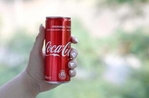 Kharkov. ukraine - 2 mai 2019, une femme caucasienne tient une boîte de conserve de coca-cola rouge avec un fond de jardin vert photo