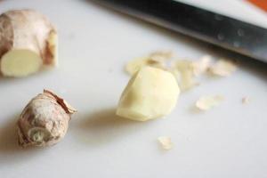 le gingembre est tranché sur une planche à découper en plastique avec un couteau sur une table orange. photo