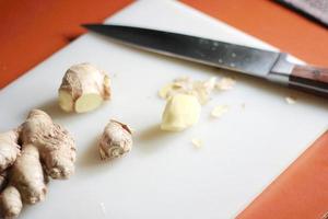 le gingembre est tranché sur une planche à découper en plastique avec un couteau sur une table orange. photo