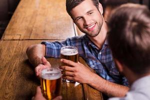 conversation amicale au bar. vue de dessus de deux jeunes hommes heureux se parlant et faisant des gestes tout en buvant de la bière au comptoir du bar photo