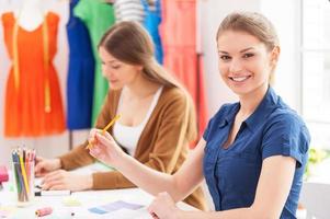 créateurs de mode confiants. belle créatrice de mode féminine regardant la caméra et souriante assise avec sa collègue photo