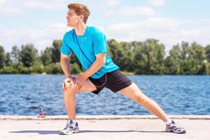 étirement à l'extérieur. beau jeune homme faisant des exercices d'étirement et souriant tout en se tenant à l'extérieur photo