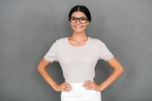 fière d'être elle-même. souriante jeune femme d'affaires tenant les mains sur les hanches et regardant la caméra en se tenant debout sur fond gris photo