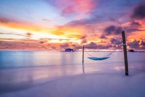 coucher de soleil sur la plage tropicale comme paysage d'été avec balançoire de plage de luxe ou hamac et villas sur l'eau et ciel de mer calme pour le paysage de plage au coucher du soleil. vacances de paysage de plage tranquille et vacances d'été photo