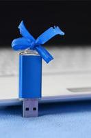 carte mémoire flash usb bleu brillant avec un arc bleu se trouve sur une couverture de tissu polaire bleu clair doux et poilu à côté d'un ordinateur portable blanc. conception de cadeau féminin classique pour une carte mémoire photo