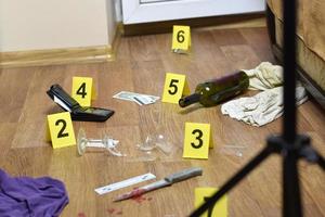 enquête sur la scène du crime - numérotation des preuves après le meurtre dans l'appartement. verre de vin cassé, couteau avec vêtements, portefeuille et bouteille comme preuve photo