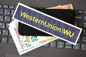 ternopil, ukraine - 6 septembre 2022 le logotype du papier western union se trouve sur un ordinateur portable noir avec des billets en euros. western union company est une multinationale américaine de services financiers photo