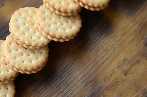 un biscuit sandwich rond fourré à la noix de coco se trouve en grande quantité sur une surface en bois marron. photo de friandises comestibles sur un fond en bois avec espace de copie